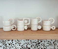 five white coffee mugs lined up on a wooden shelf in front of a wall