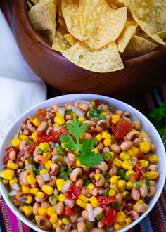 a white bowl filled with corn and salsa next to tortilla chips on a colorful table cloth