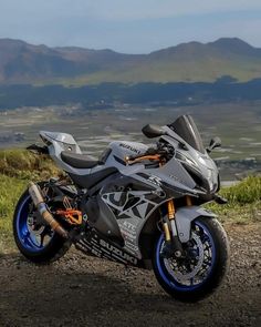 a motorcycle parked on the side of a dirt road next to grass and mountains in the background