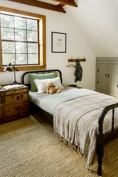 a bed with a teddy bear on it in a bedroom next to a dresser and window