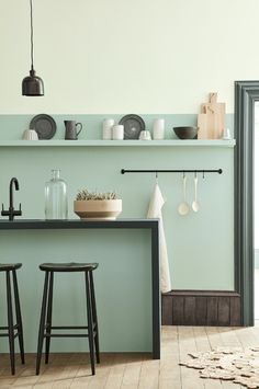 a kitchen with green walls and wooden flooring, two stools in front of the counter