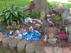 a garden with rocks, plants and fairy houses in the ground next to a tree