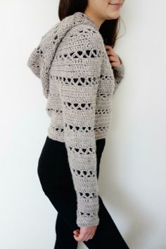 a woman standing in front of a white wall wearing a gray crocheted hoodie