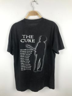 a black t - shirt that says the cure with a man standing in front of it