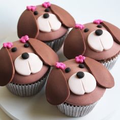 four cupcakes with chocolate frosting and white icing decorated to look like dogs