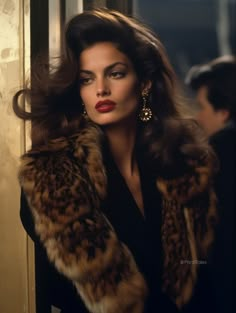 a woman with long hair wearing a fur coat and gold earrings, standing in front of a window