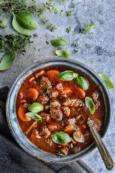 a bowl filled with meat and vegetables next to some green leaves on top of a table