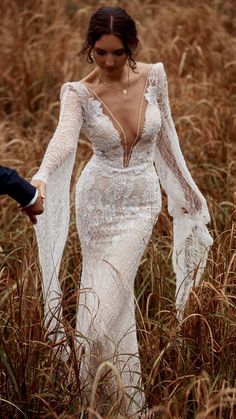 a woman in a white wedding dress walking through tall grass with her arms around her body