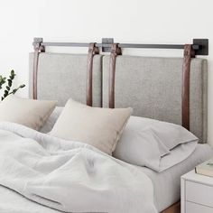 an unmade bed with white linens and wooden headboard, in a bedroom