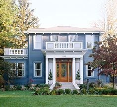 a blue house with white trim and two story windows on the second floor is surrounded by lush green grass