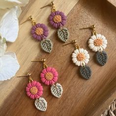 four flower shaped earrings on top of a wooden table next to white and pink flowers