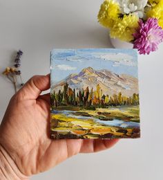 a person holding up a small painting in their hand