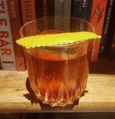 a close up of a drink in a glass on a table with books behind it