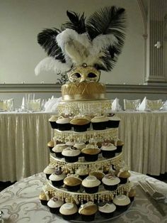 a three tiered cake with cupcakes and feathers on the top is decorated in black, white and gold