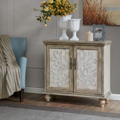 a white cabinet sitting next to a blue chair and vase with flowers on top of it