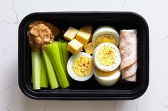 a black container filled with eggs, celery and other food on top of a white counter