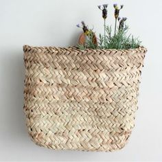 a woven basket with flowers in it hanging on the wall next to a planter