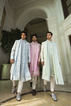 three men standing next to each other in front of a doorway wearing white and pink outfits