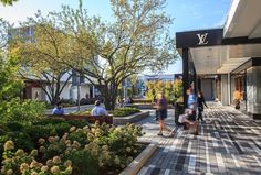 people are walking on the sidewalk in front of shops and buildings with trees around them