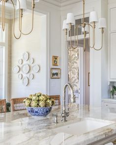 a bowl of flowers is sitting on the kitchen island in this white and gold home