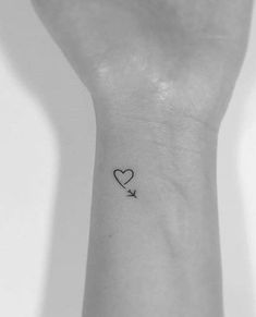 a small tattoo on the wrist of a woman with a heart and an arrow in it