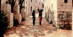 two people walking down an alley way with their arms in the air and one person holding up her head