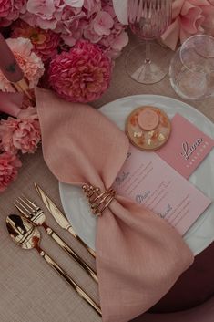 the table is set with pink flowers and gold place settings