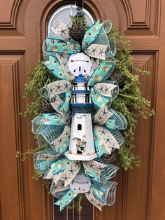 a wreath with a lighthouse on it hanging from the front door, decorated with blue and white ribbons