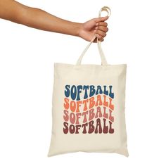 a hand holding a white tote bag that says softball