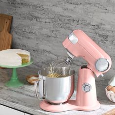 a pink mixer sitting on top of a counter next to other kitchen accessories and food