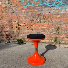 an orange stool sitting in front of a brick wall with graffiti on it's side