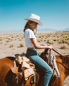 a young woman riding on the back of a brown horse in an open desert area