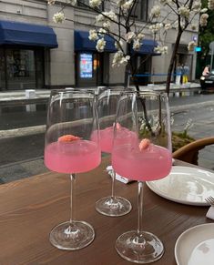 two wine glasses filled with pink liquid sitting on top of a wooden table next to a white plate