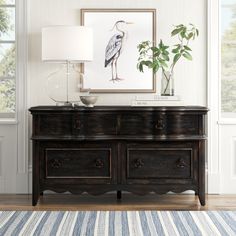 a living room with a large painting on the wall next to a dresser and lamp