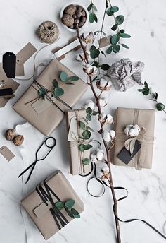 some wrapping paper and scissors on a marble table with eucalyptus branches, cotton floss and other items