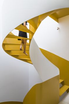 a person standing on the top of a yellow and white spiral stair case in a building