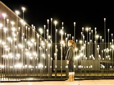 a woman standing next to a fence with lots of lights on it