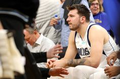 a basketball player sitting on the floor with his hands in his pockets and other people standing around him