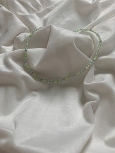 a beaded necklace laying on top of a white cloth covered bed sheet with sheets in the background