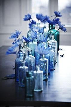 there are many blue vases with flowers in them on the table next to each other