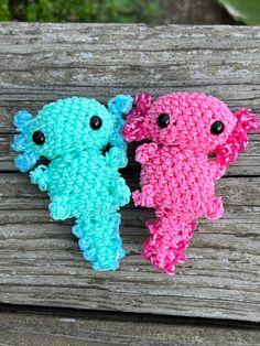 two crocheted stuffed animals sitting next to each other on a wooden bench with grass in the background