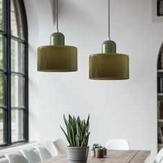 two green lamps hanging from the ceiling above a wooden table with chairs and a potted plant