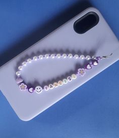 a cell phone case with a beaded name and smiley face on the front, sitting on a blue surface