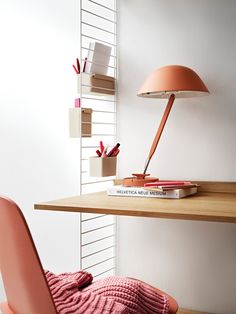 a pink chair sits in front of a desk with a lamp and books on it