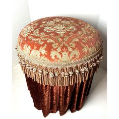 an orange and gold ottoman with tassels on the top, sitting against a white wall