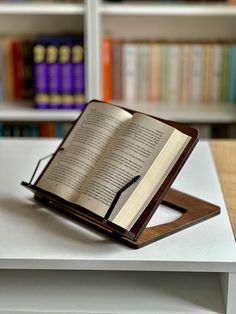 an open book sitting on top of a white table next to bookshelves in a library