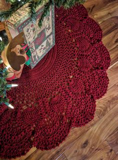 a red crocheted doily on the floor next to a christmas tree and presents