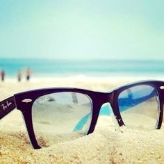 a pair of sunglasses sitting on top of a sandy beach next to the ocean with people in the background