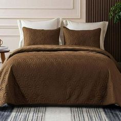 a bed with brown comforter and pillows on top of it in a room next to a table