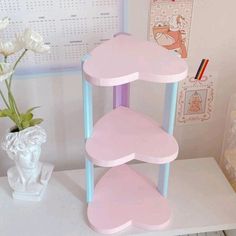 a pink and blue three tiered shelf next to a white vase with flowers in it